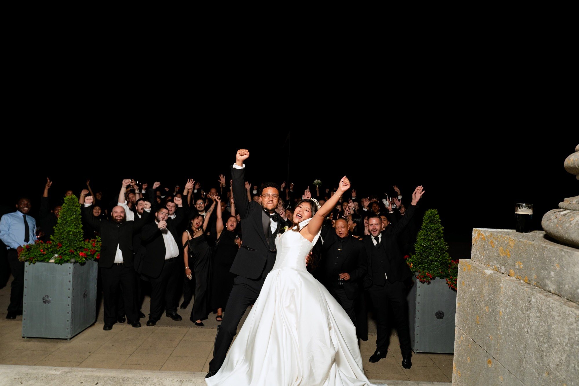 Bride and groom cheering with their guests at night outside the venue