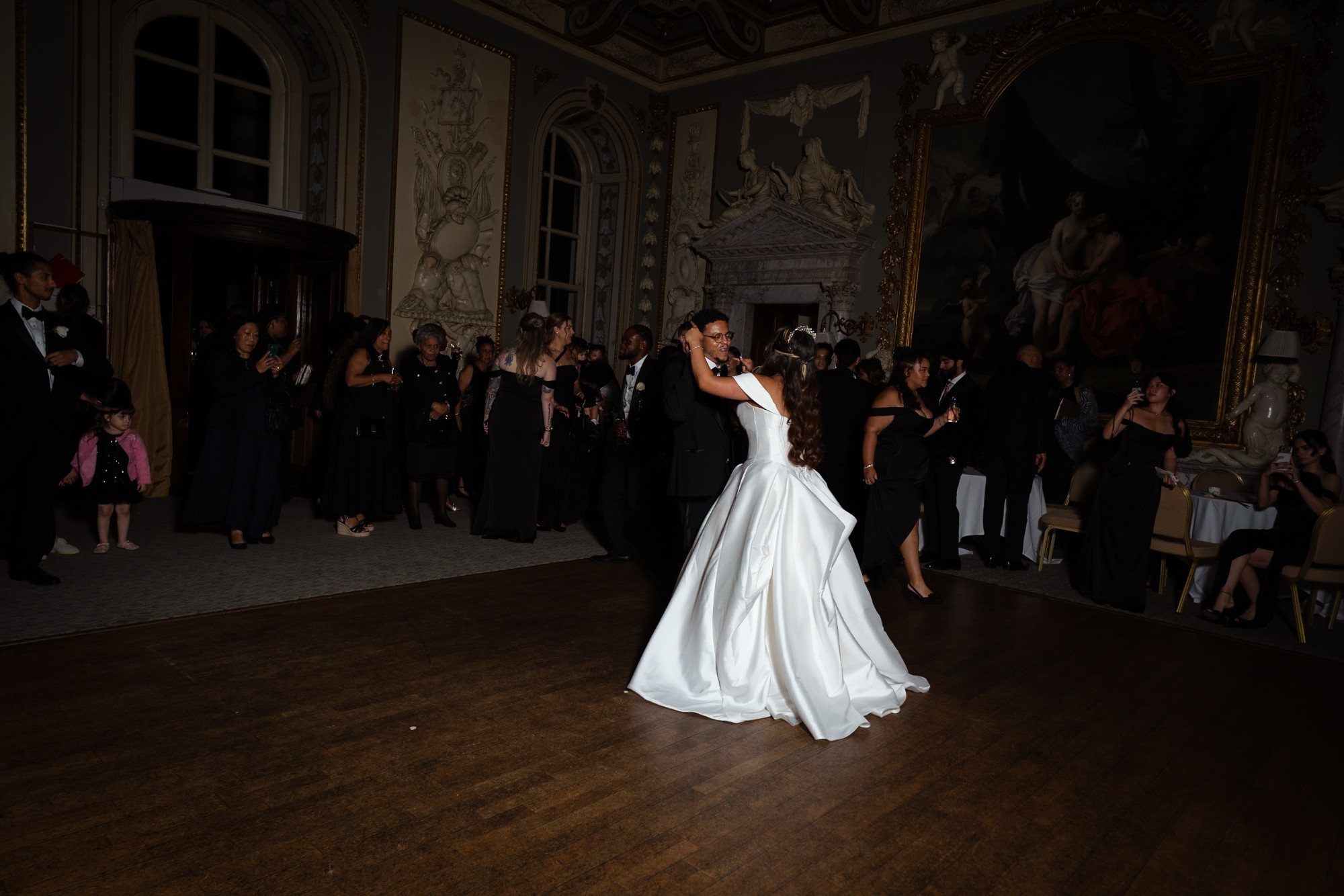 Bride and groom dancing in a candlelit ballroom while guests watch