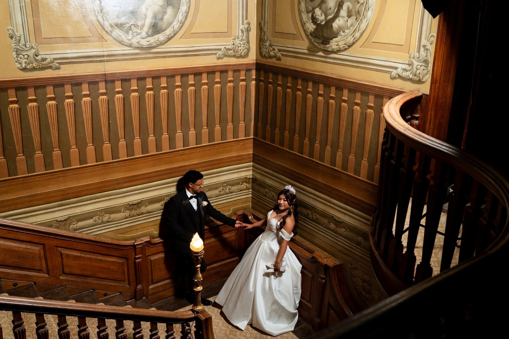 Bride and groom holding hands on a grand painted staircase
